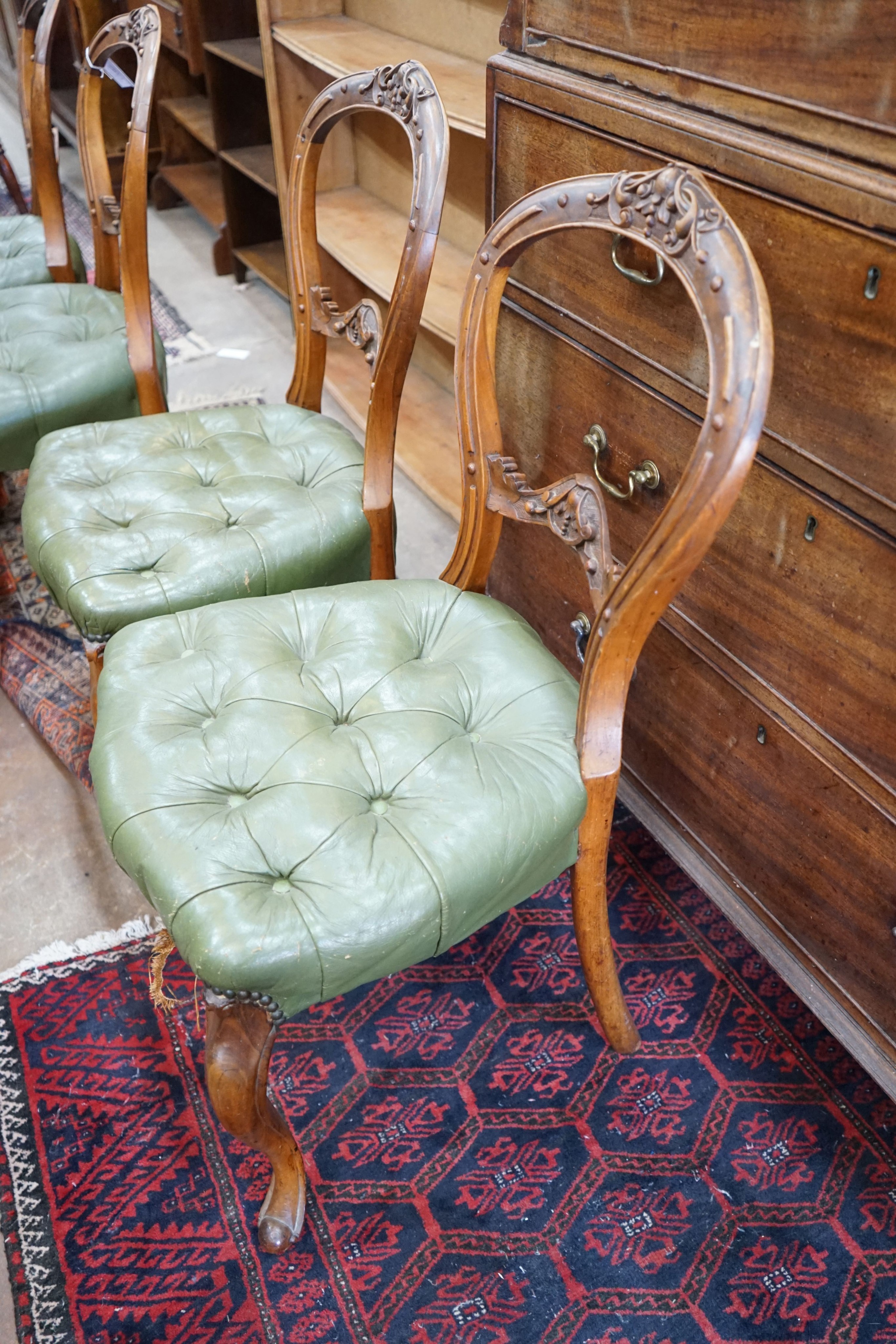 A set of six Victorian carved walnut and buttoned green leather spoon back dining chairs